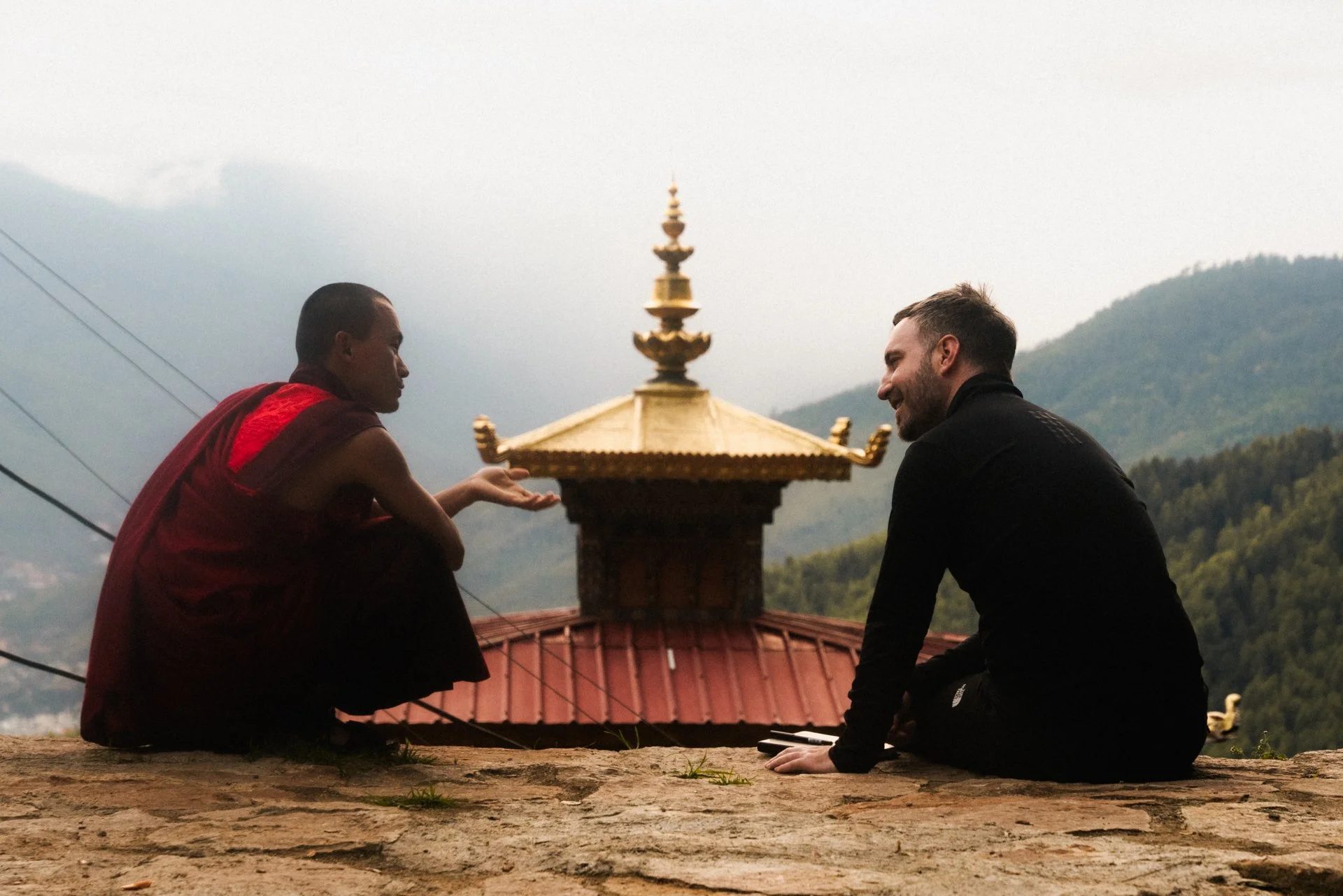 A monk and a traveller in conversation beside a golden temple roof