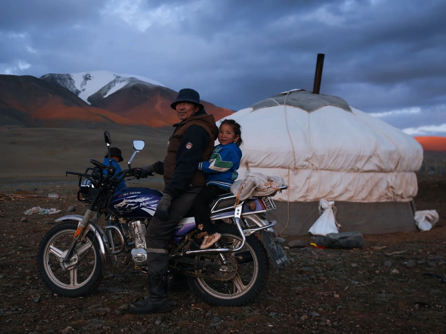 A grandfather and granddaughter on a motorbike beside their ger