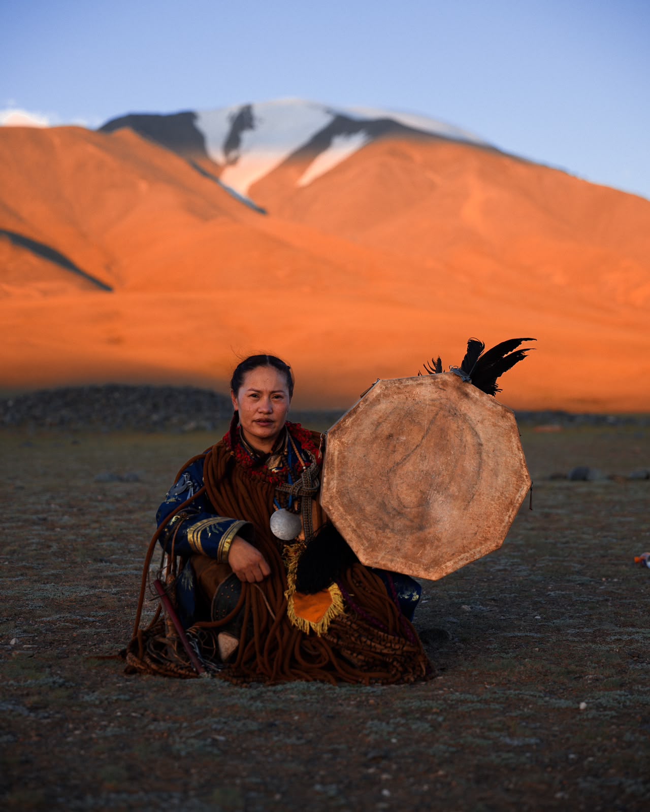 A female shaman with her drum before the glowing mountains