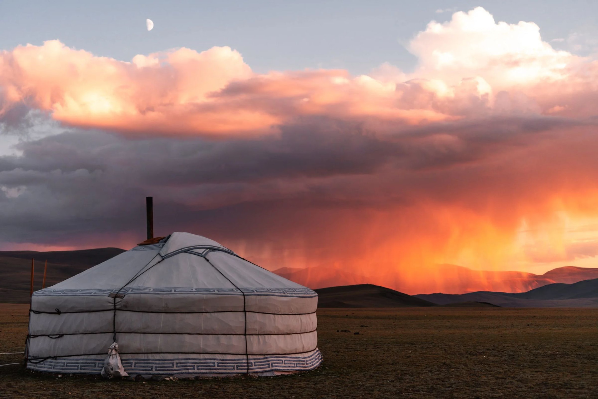 A ger beneath a storm lit orange at sunset
