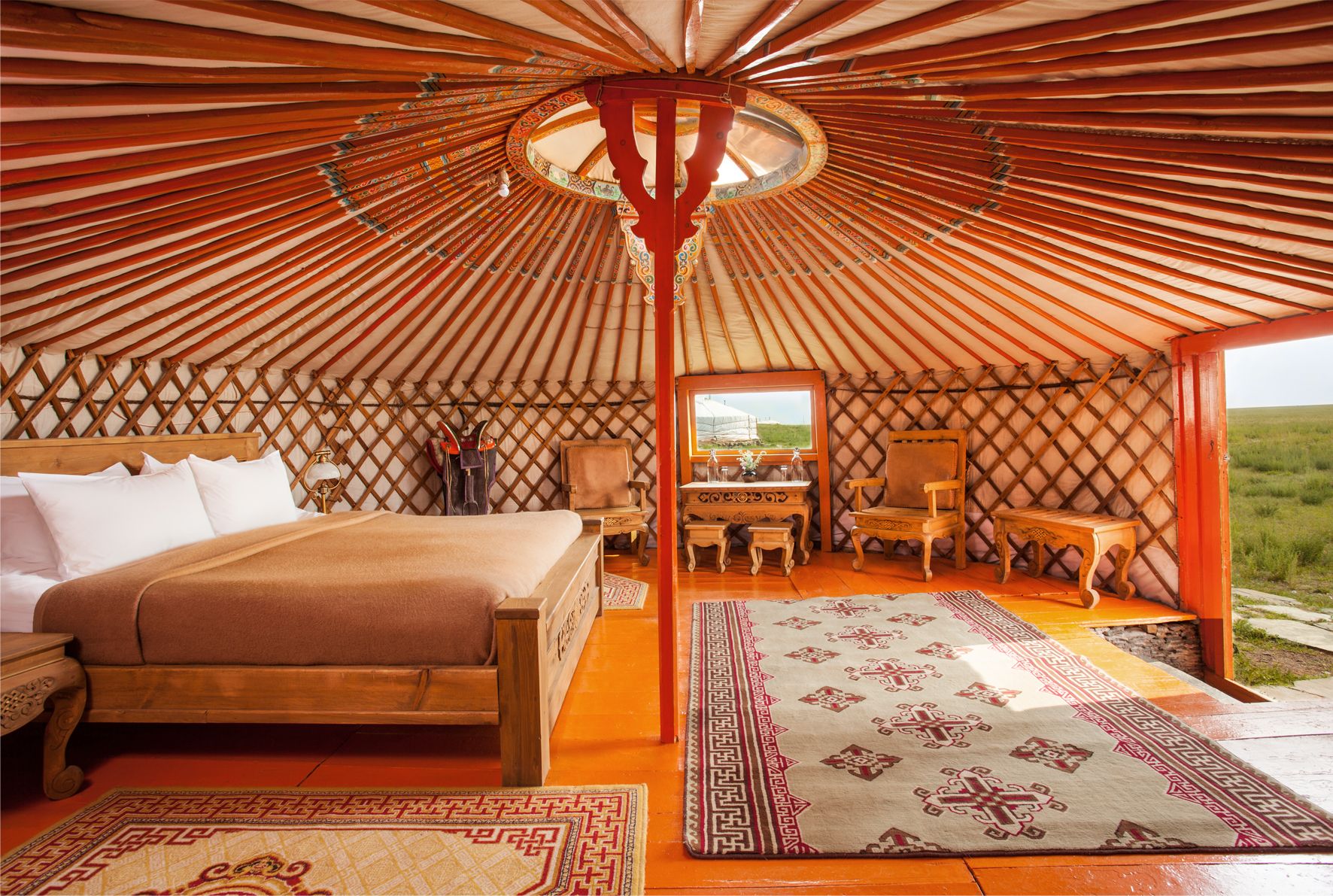 A ger suite with a king bed and carved wooden furniture
