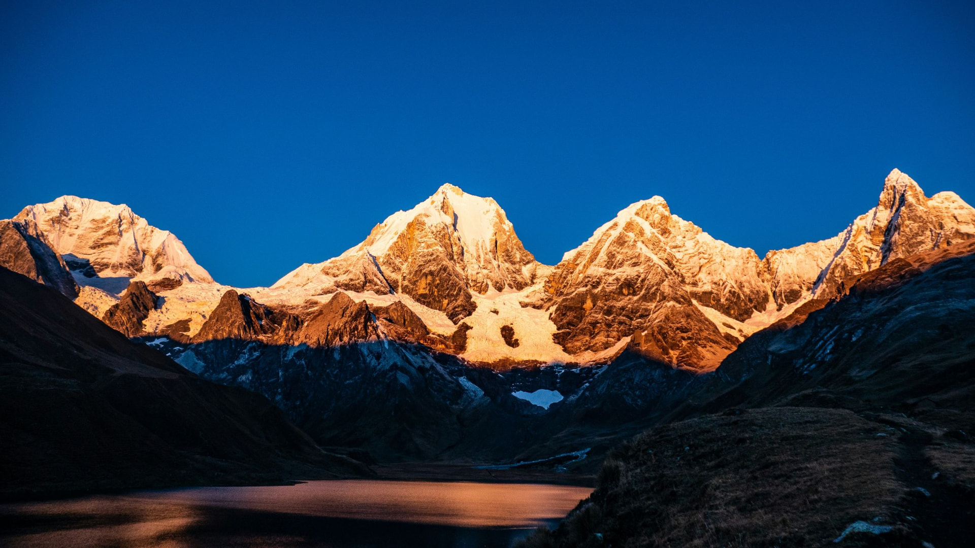 Snow peaks glowing at dawn above a high lake